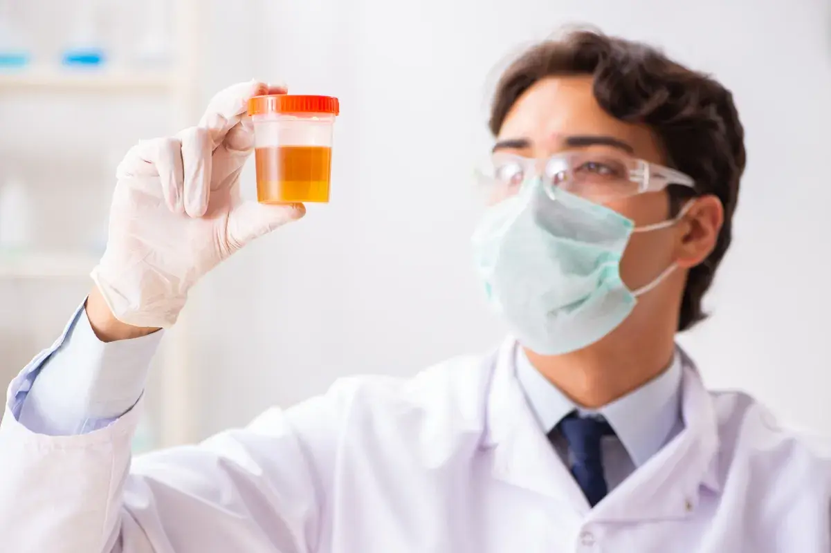 Clinician in a mask inspects a liquid laboratory sample.